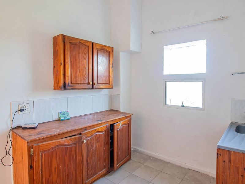 A dated kitchen area featuring wooden cabinetry, a stainless steel sink, and tiled splashbacks, offering a blank canvas for renovation.