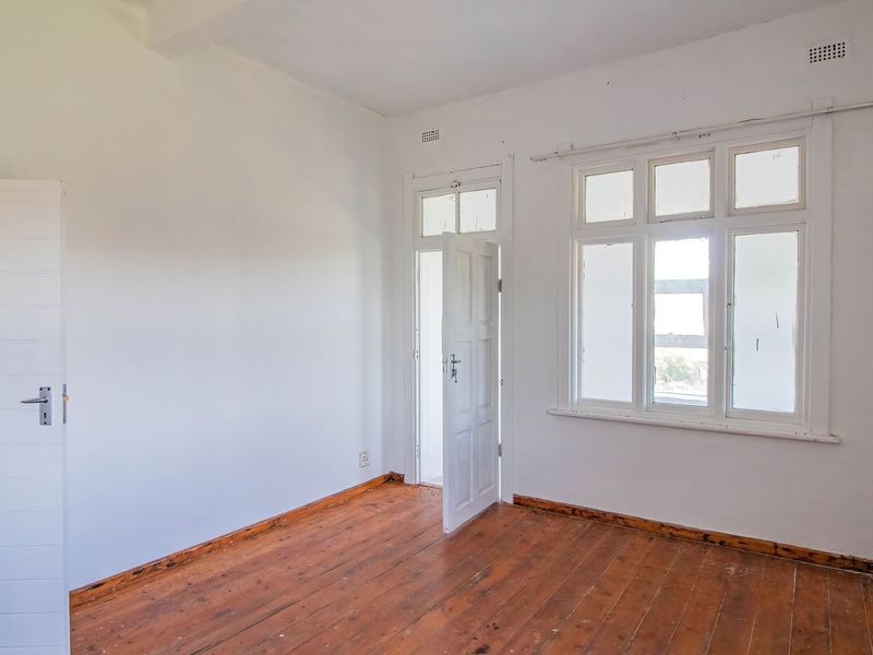 An empty bedroom featuring original timber flooring, white walls, and multi-pane windows, offering a blank canvas for renovation or interior design.