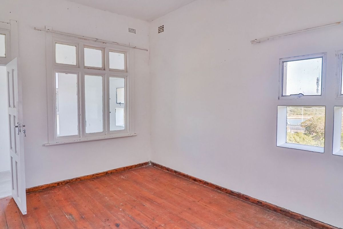 An empty bedroom featuring original timber flooring and multiple casement windows, offering a blank canvas for renovation and interior design updates.