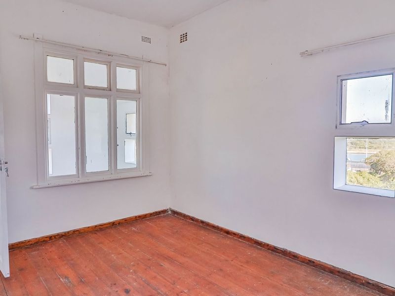 An empty bedroom featuring original timber flooring and multiple casement windows, offering a blank canvas for renovation and interior design updates.