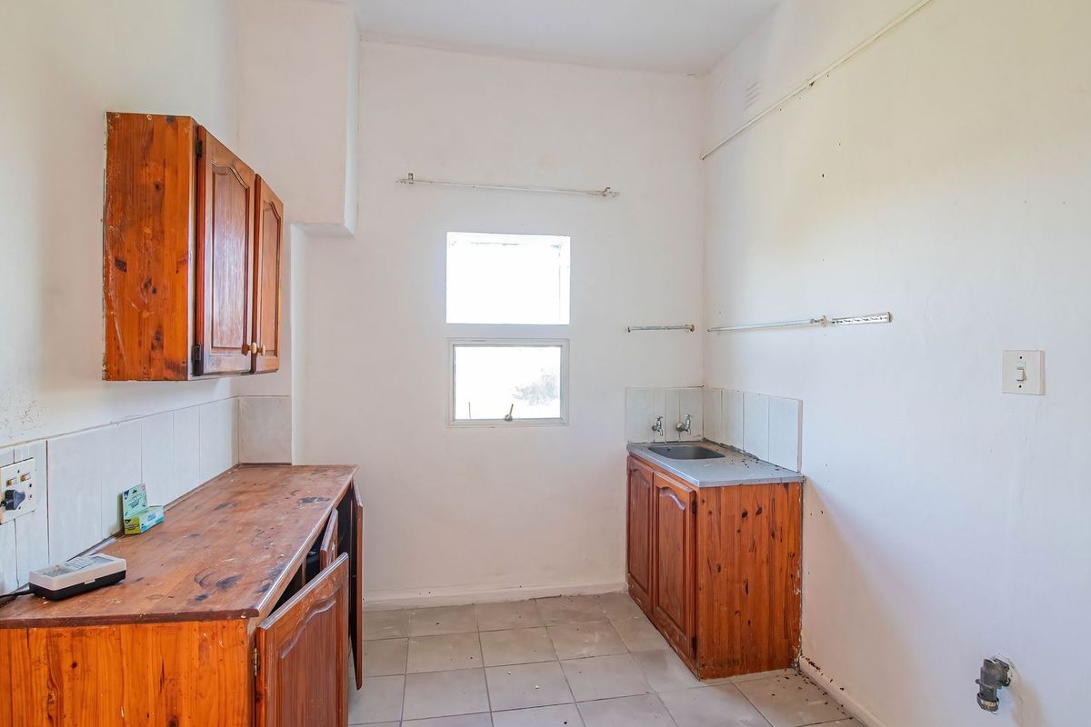 A dated kitchen area featuring timber cabinetry, a stainless steel sink, and tiled flooring, offering significant potential for renovation and modernization.