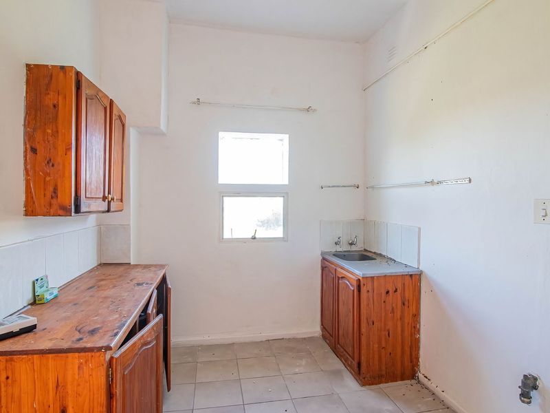 A dated kitchen area featuring timber cabinetry, a stainless steel sink, and tiled flooring, offering significant potential for renovation and modernization.