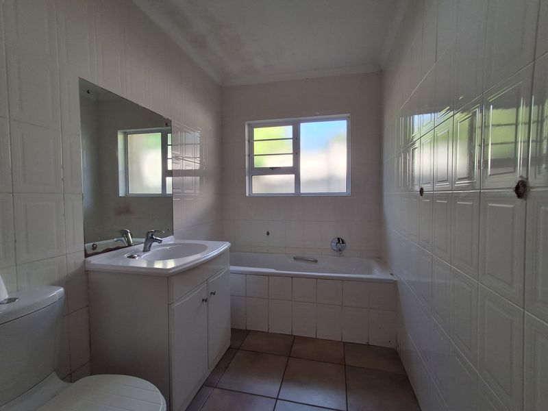 A functional bathroom featuring a built-in vanity, bathtub, and tiled finishes, offering a clean canvas for potential modern updates.