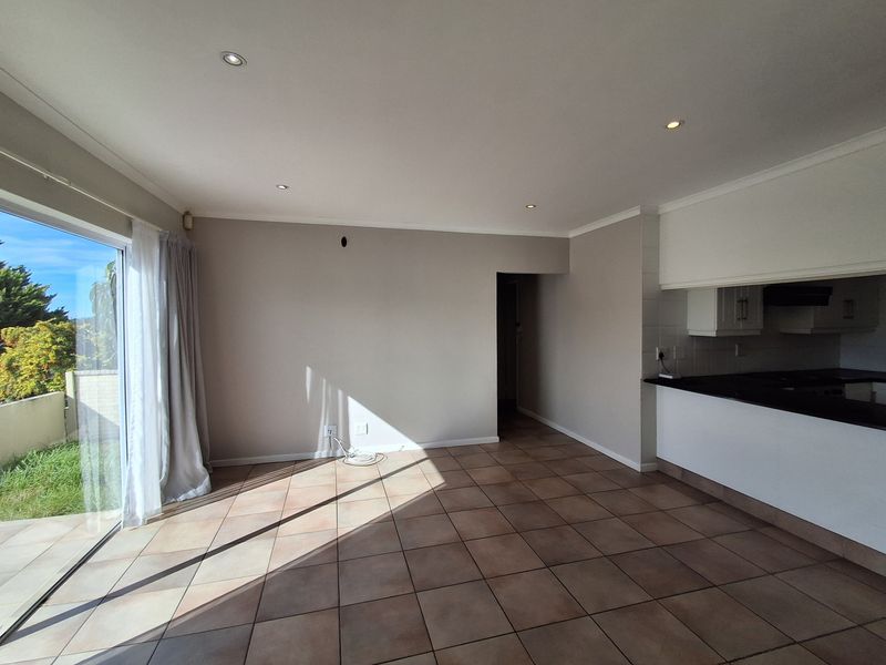 An open-plan living and kitchen area featuring tiled flooring, recessed lighting, and a large sliding glass door providing access to the garden.