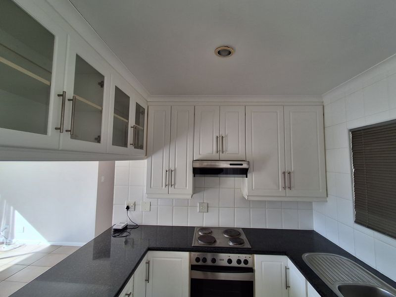 A clean, functional kitchen featuring white cabinetry, dark granite countertops, a built-in oven, electric hob, and a tiled backsplash.