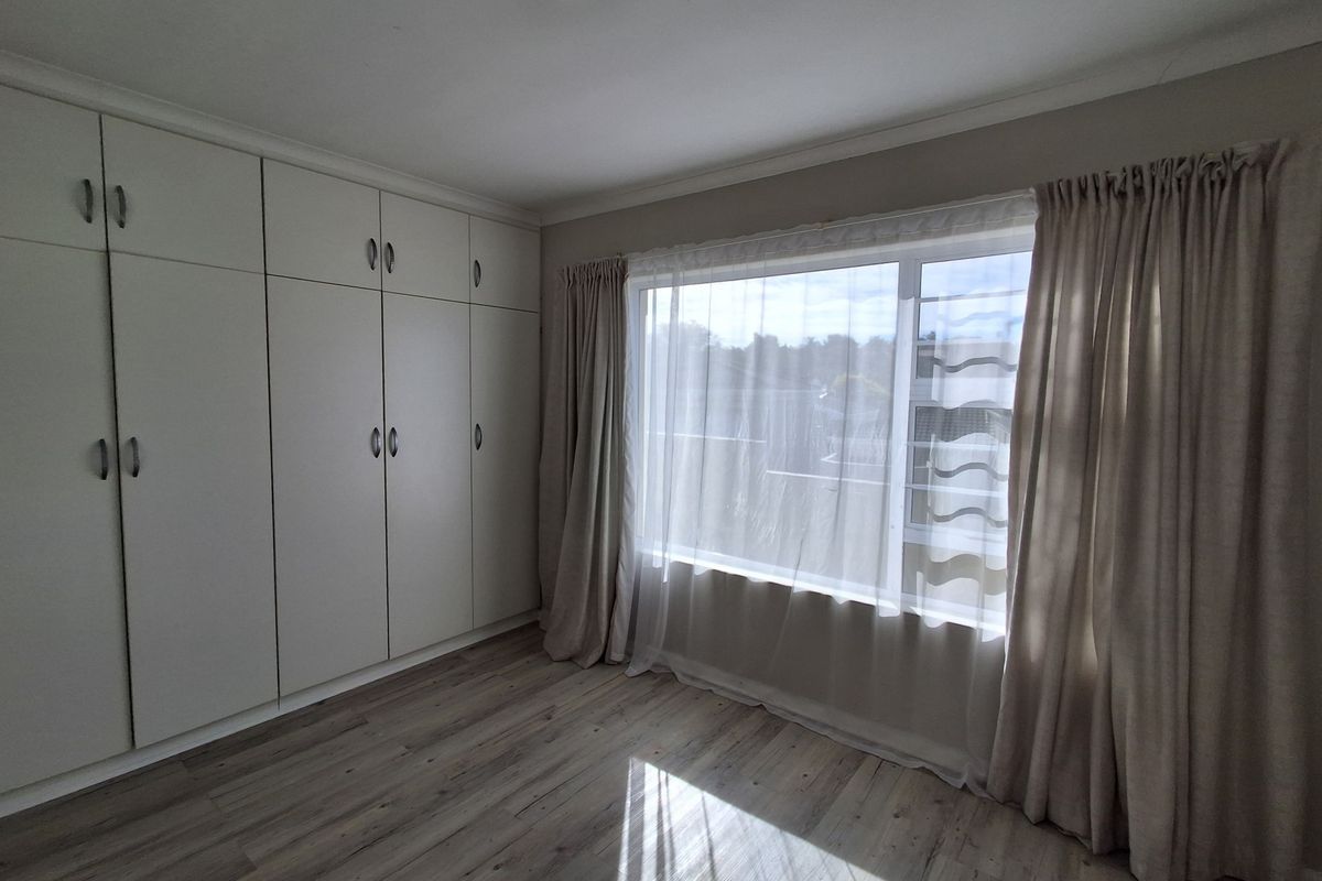 A bright and spacious bedroom featuring modern laminate flooring, ample built-in cupboard storage, and large windows allowing for plenty of natural light.