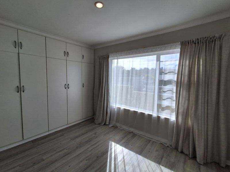 A bright and spacious bedroom featuring modern laminate flooring, ample built-in cupboard storage, and large windows allowing for plenty of natural light.