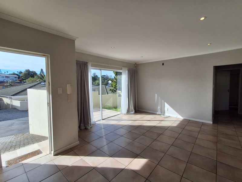 Spacious, light-filled living area featuring neutral tiled flooring, recessed downlighting, and direct access to an outdoor patio through sliding glass doors.
