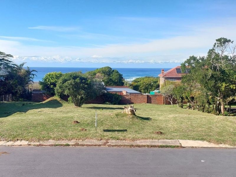 A vacant residential plot featuring a grass lawn, boundary wall, and scenic ocean views from the street frontage.