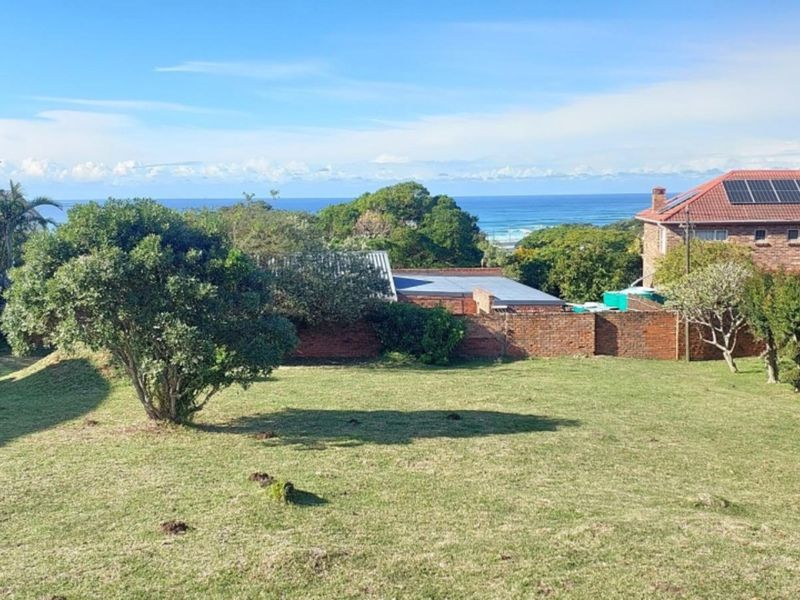 A scenic view of the ocean and surrounding landscape from the vacant residential property, featuring established trees and a brick boundary wall.