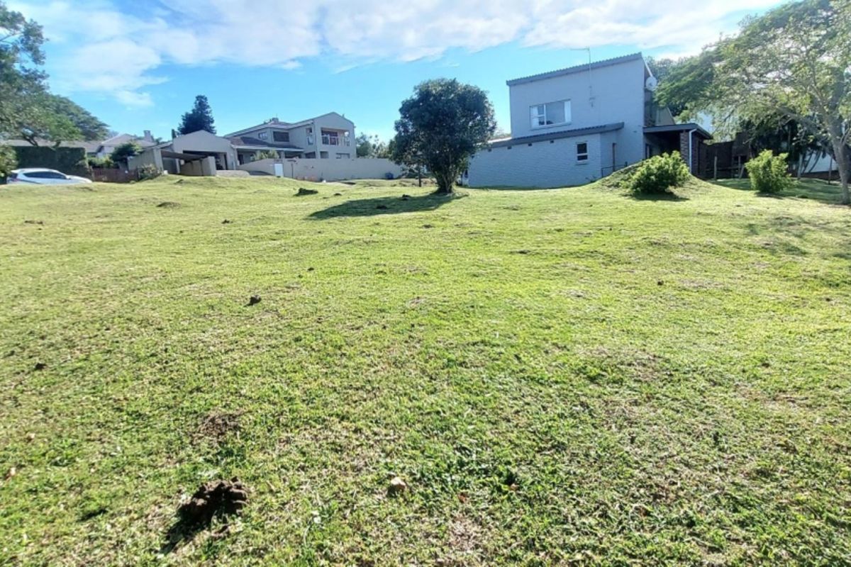 A spacious, gently sloping grass plot with mature trees, offering a clear view of neighboring residential properties.
