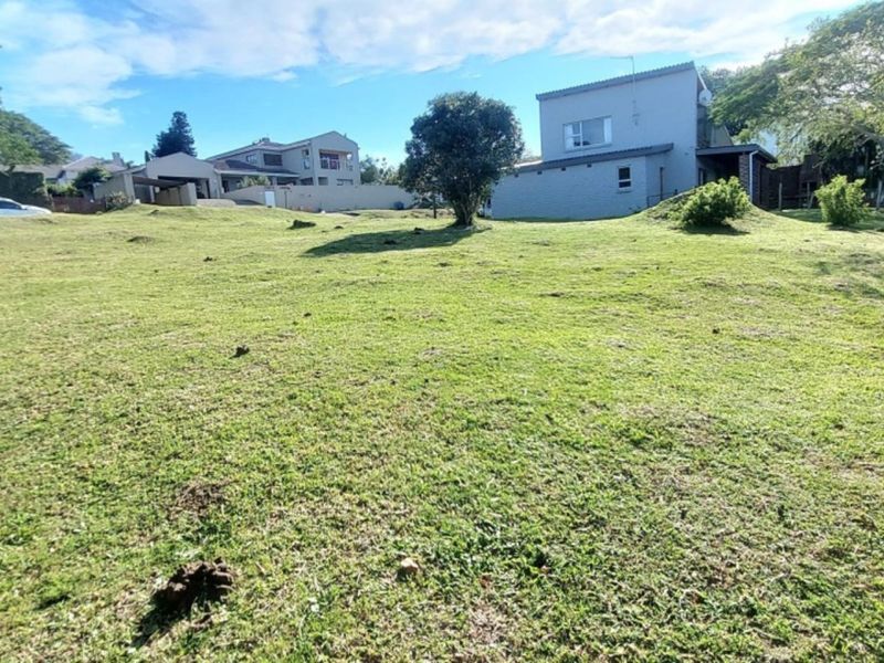 A spacious, gently sloping grass plot with mature trees, offering a clear view of neighboring residential properties.