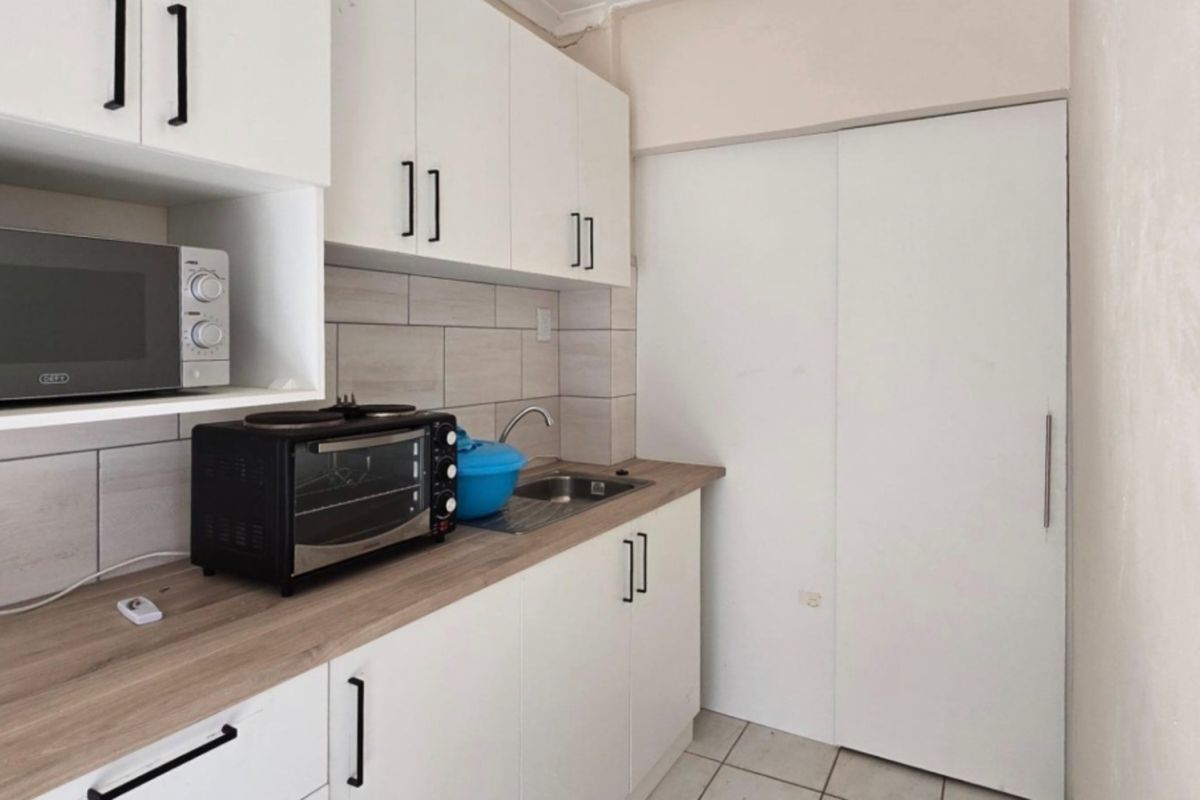 A compact, modern kitchen featuring white cabinetry, wood-look laminate countertops, a tiled backsplash, and neutral floor tiles.