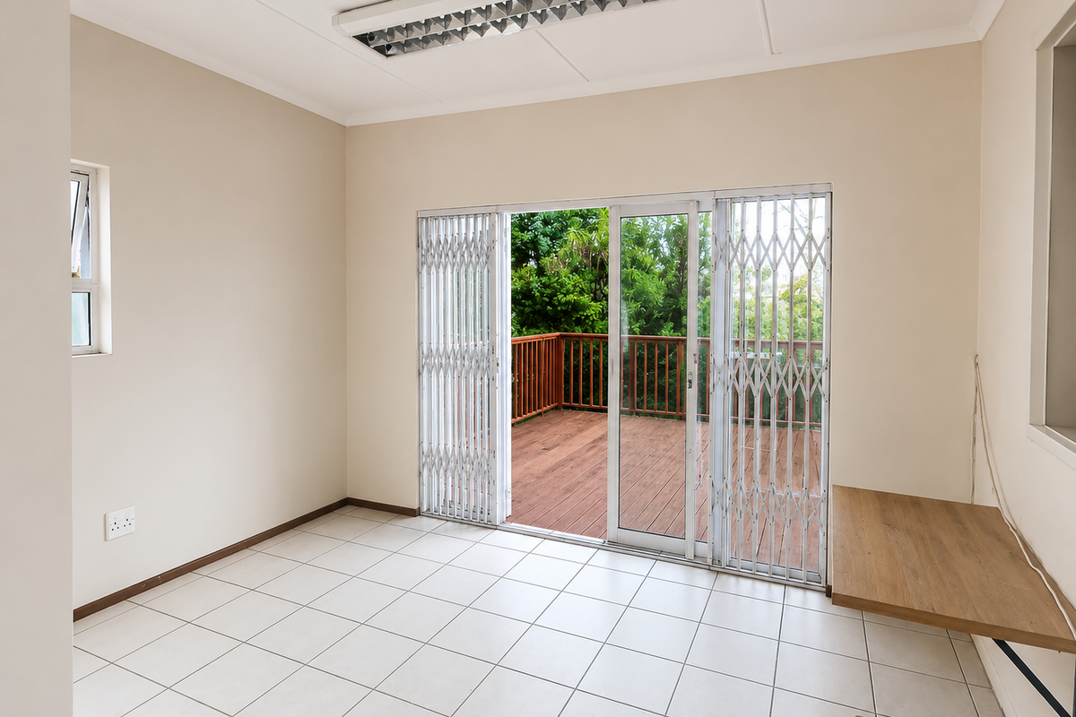 An empty living room featuring tiled floors, a built-in desk, and sliding glass doors opening onto a wooden deck.