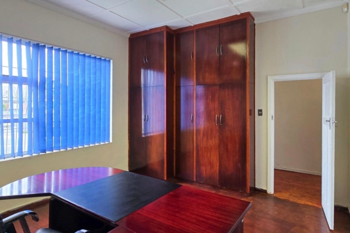 Bedroom featuring built-in wooden cupboards, vertical blinds, and wooden flooring.