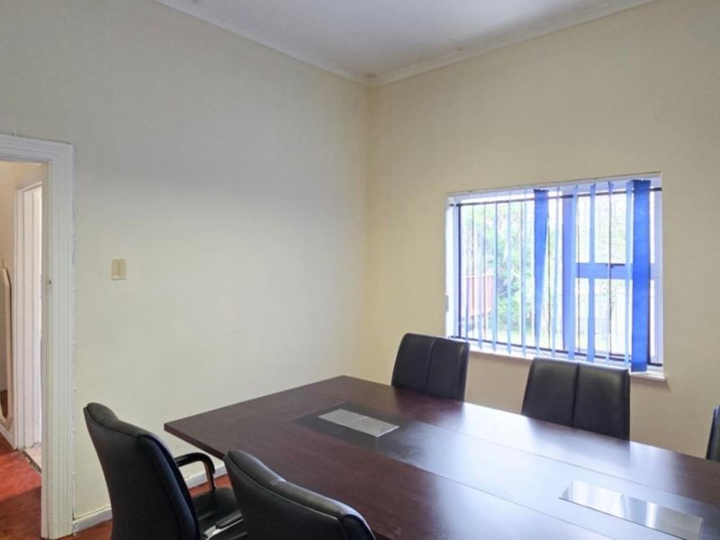 A functional office space featuring timber flooring, neutral walls, and vertical window blinds, suitable for a home workspace or study.