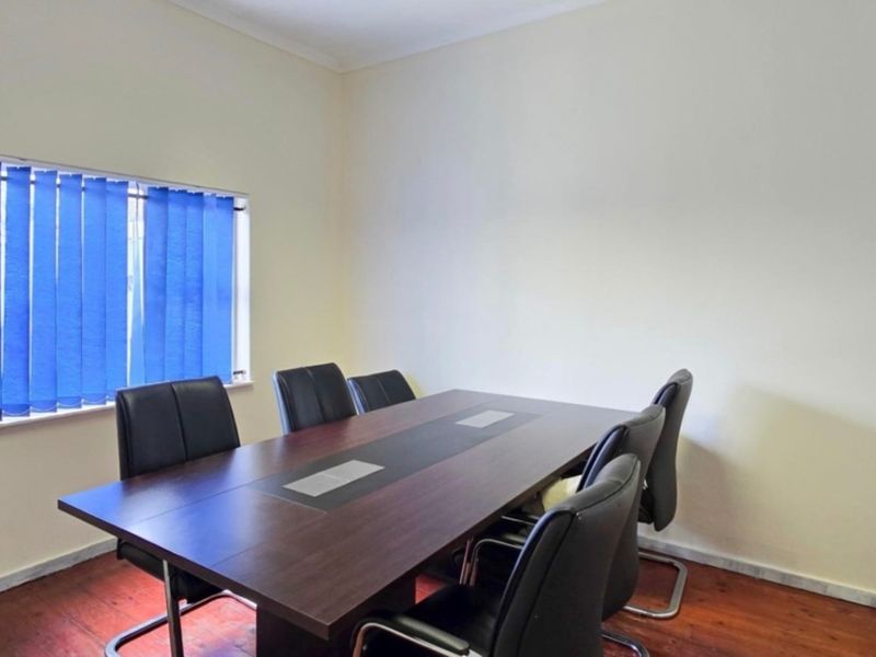 A functional office space featuring timber flooring and a window with vertical blinds, suitable for a home workspace or study.