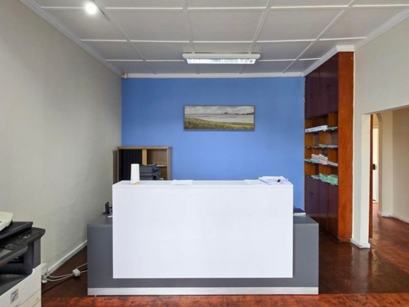 A functional office space featuring built-in wooden shelving, a tiled ceiling, and hardwood flooring, currently set up with a reception desk.