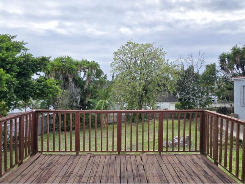 An elevated wooden deck featuring a timber balustrade, overlooking a rear garden area with mature trees and a neighboring property.