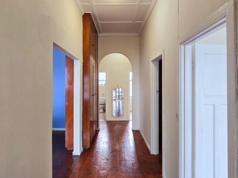 A spacious hallway featuring original hardwood flooring, built-in storage cabinetry, and a classic architectural archway leading toward the rear of the home.