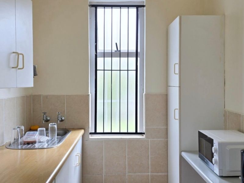 A functional scullery area featuring built-in white cabinetry, a stainless steel sink, tiled splashbacks, and a window with security bars.