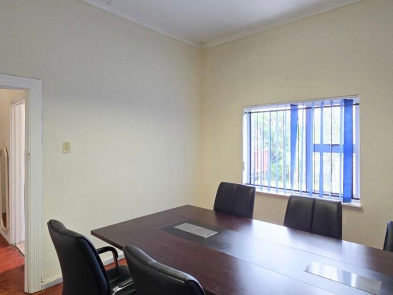 A functional office space featuring timber flooring, neutral walls, and vertical blinds, suitable for a home workspace or study.