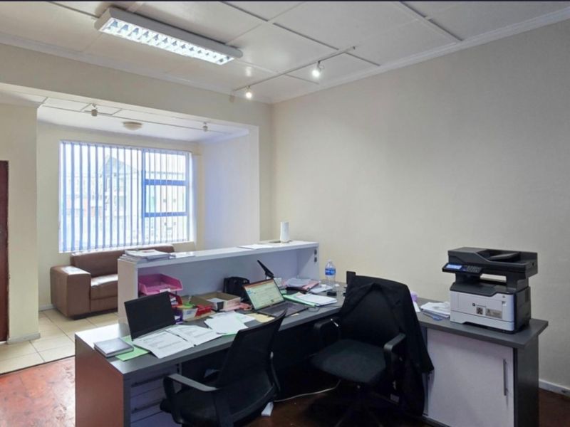 A functional office space featuring tiled flooring, vertical blinds, and overhead fluorescent lighting, suitable for a professional workspace or home study.