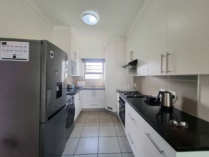 A functional galley-style kitchen featuring white cabinetry, dark granite countertops, tiled backsplash, and integrated appliances including an oven and extractor fan.