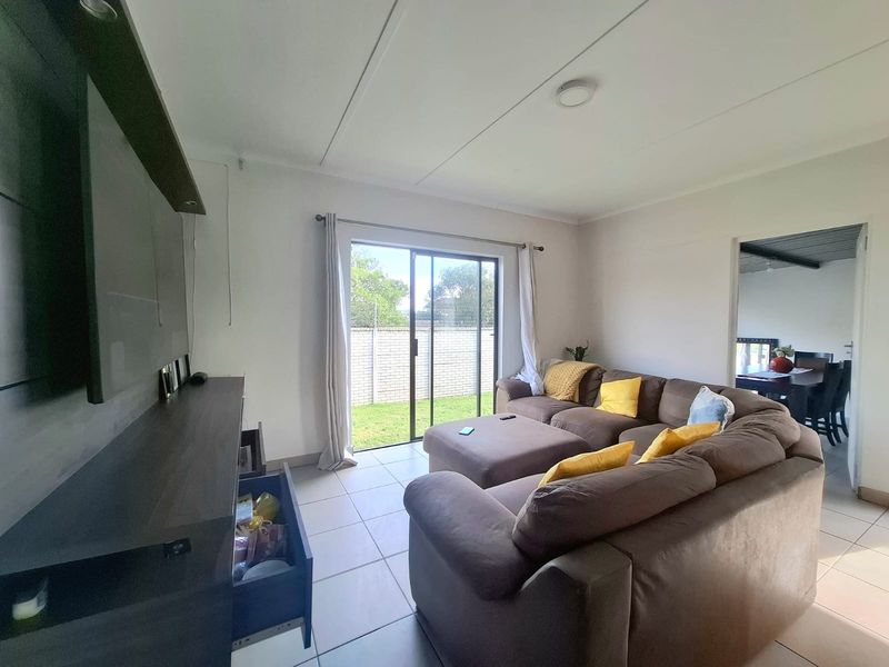 A bright living room featuring tiled flooring and a sliding glass door providing access to the rear garden area.