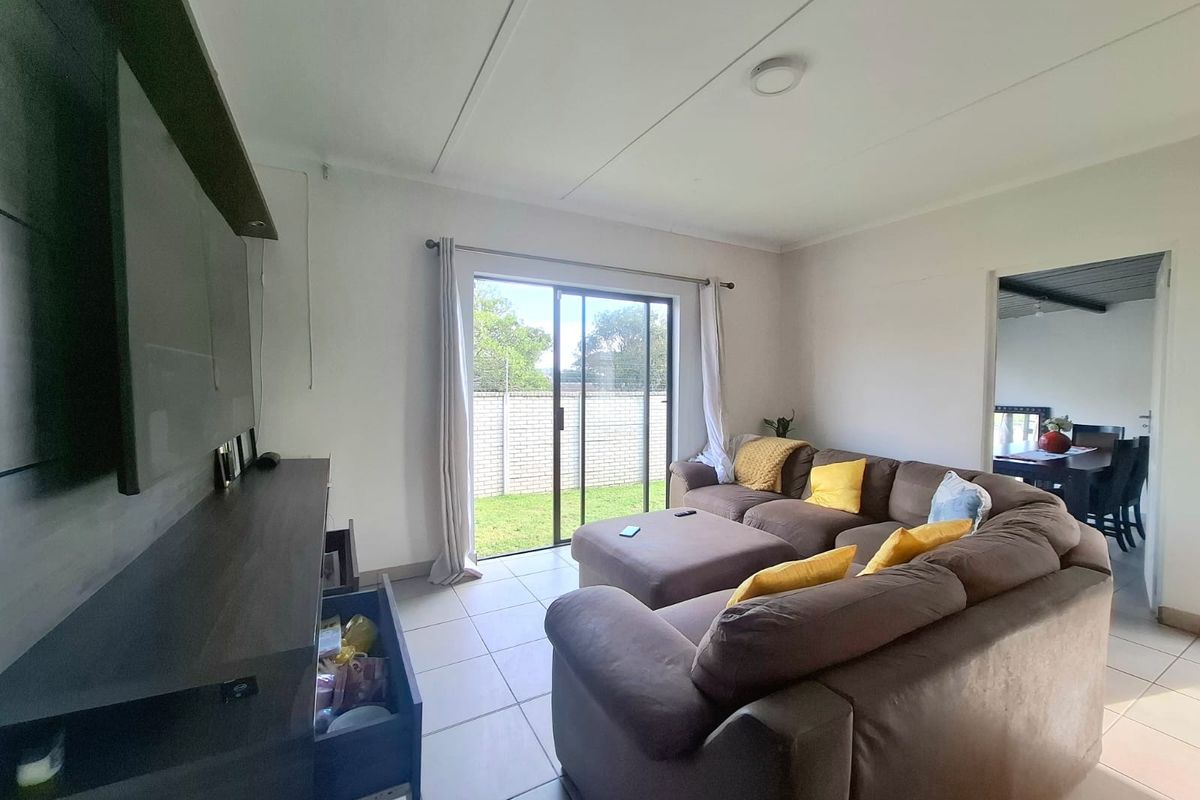 A bright living room featuring tiled flooring and a sliding glass door providing access to the rear garden area.