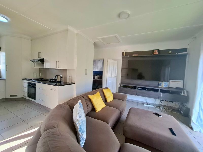 Open-plan living area featuring a modern kitchen with granite countertops, built-in oven, and hob, seamlessly flowing into a comfortable lounge space with tiled flooring.