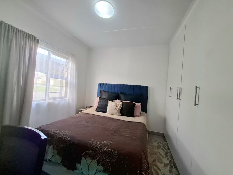 A well-maintained bedroom featuring built-in cupboards, tiled flooring, and a large window allowing for natural light.
