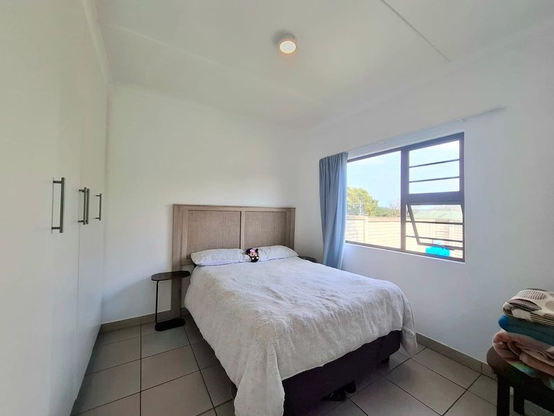 A functional bedroom featuring tiled flooring, built-in cupboards, and an aluminium window frame providing natural light.