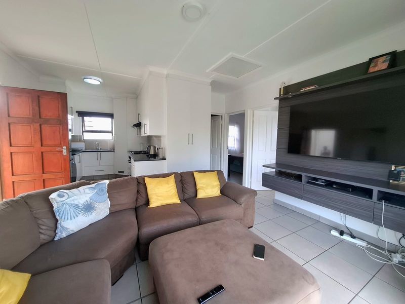 Open-plan living area featuring tiled flooring, a built-in media unit, and an adjacent kitchen with white cabinetry and sink.