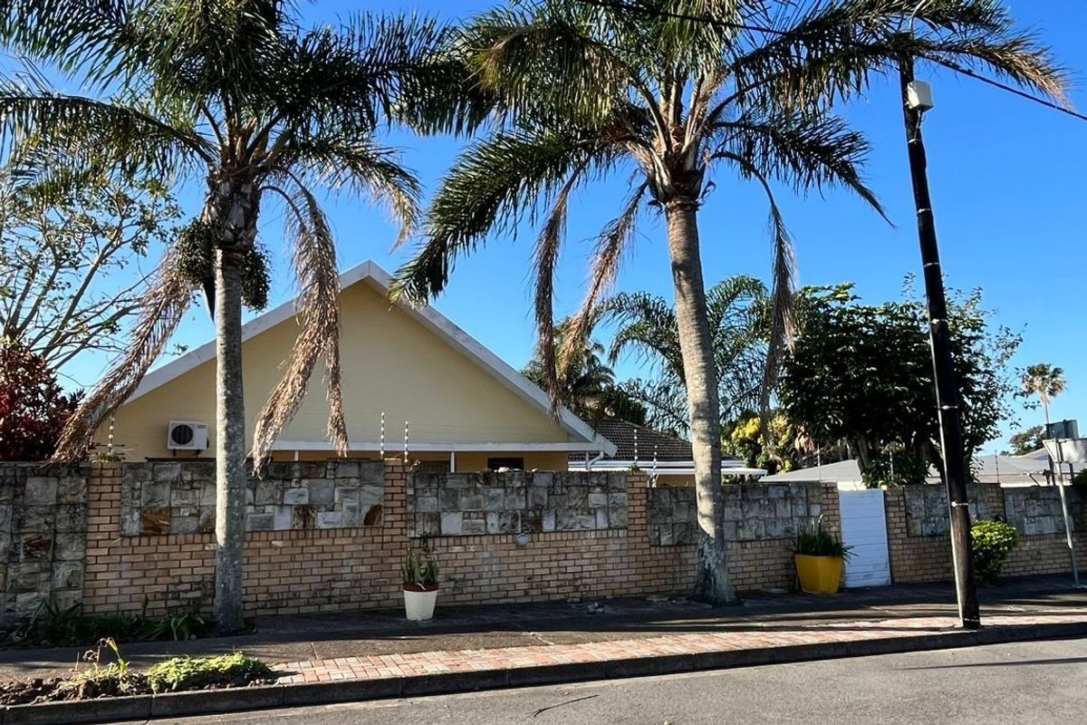 Street view of the property featuring a stone and brick boundary wall with electric fencing and mature palm trees.