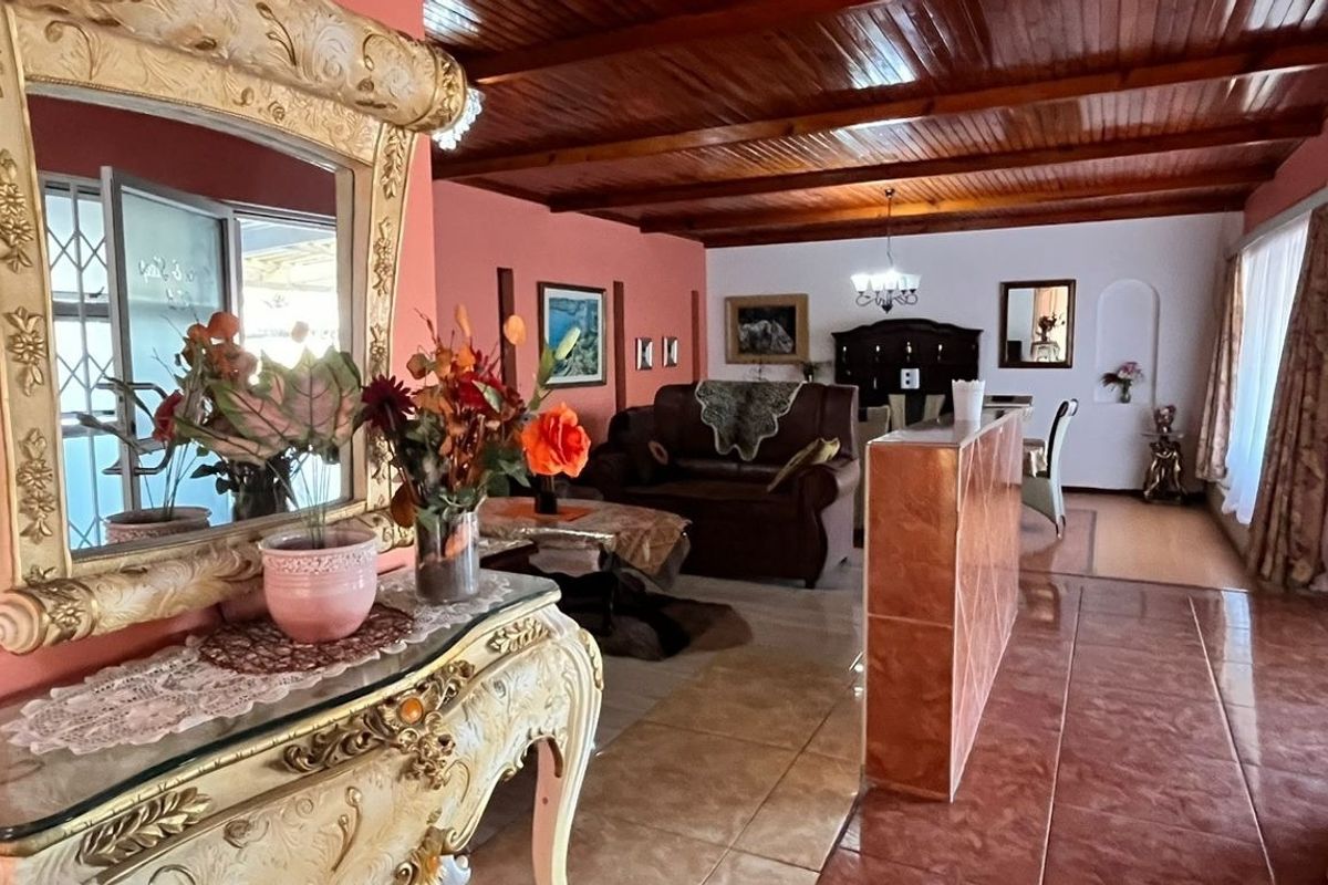Open-plan living and dining area featuring exposed timber beam ceilings, tiled flooring, and a central partition wall.