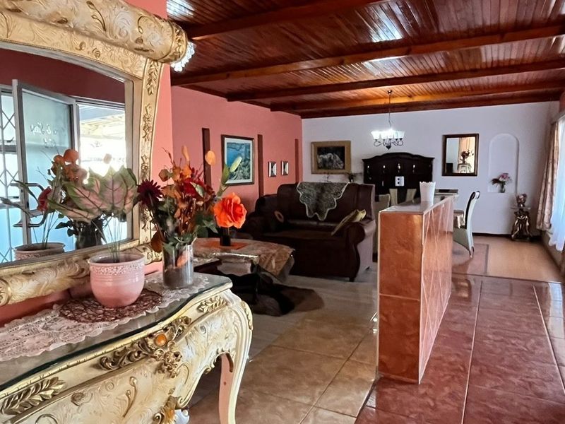 Open-plan living and dining area featuring exposed timber beam ceilings, tiled flooring, and a central partition wall.