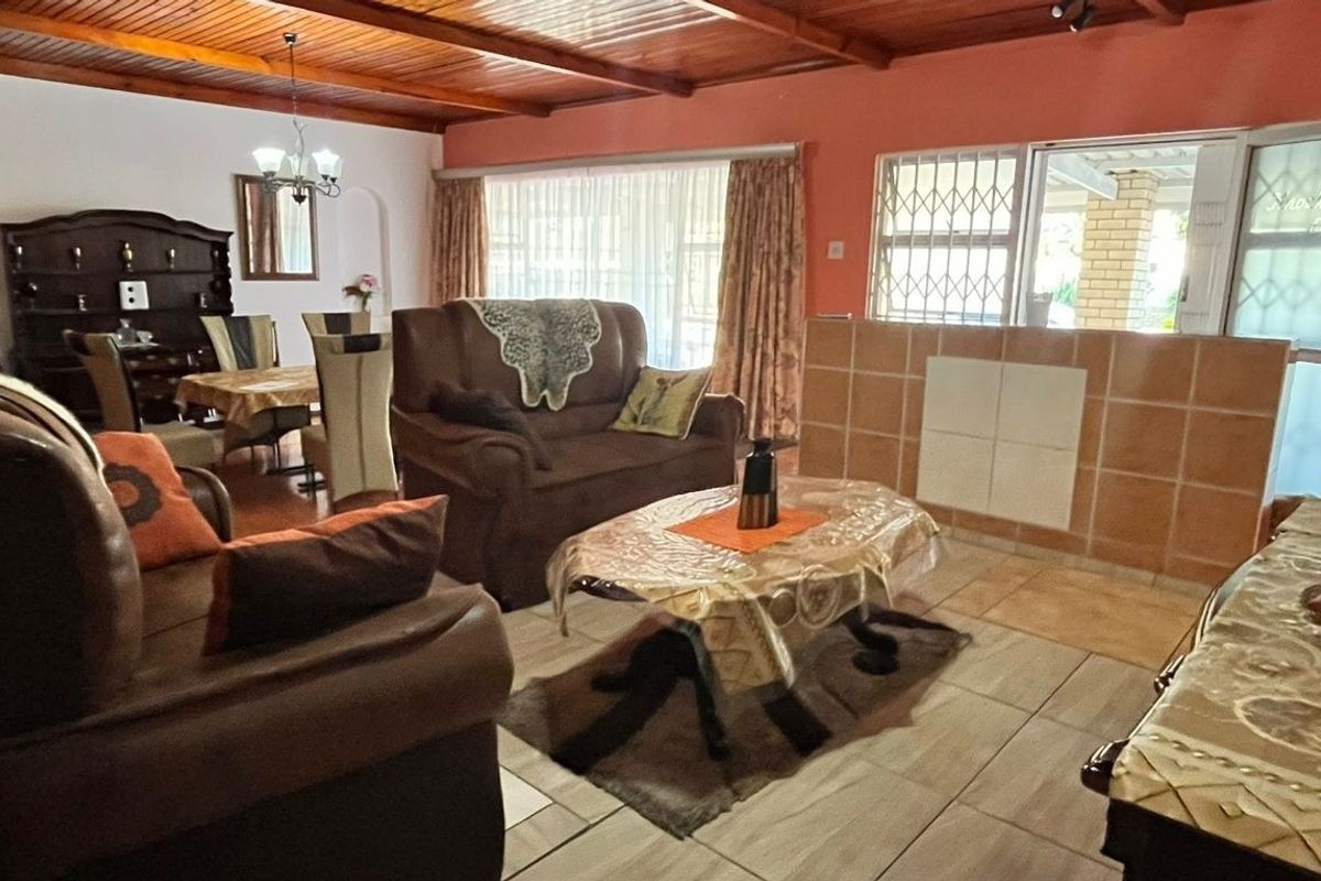 Open-plan living and dining area featuring exposed timber beam ceilings, tiled flooring, and a tiled partition wall with access to the exterior.