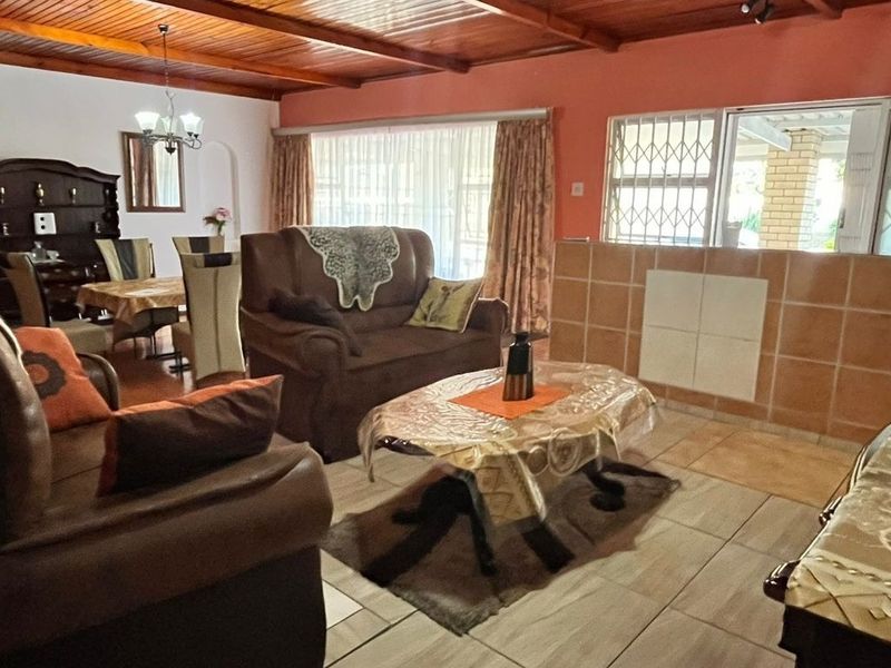 Open-plan living and dining area featuring exposed timber beam ceilings, tiled flooring, and a tiled partition wall with access to the exterior.