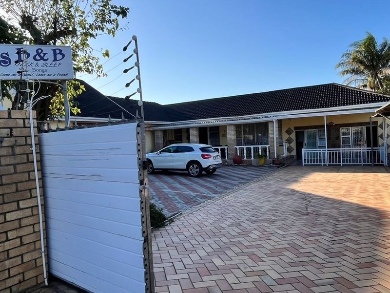 Front exterior view of the guest house featuring paved driveway, secure gated entrance, electric fencing, and covered parking area.