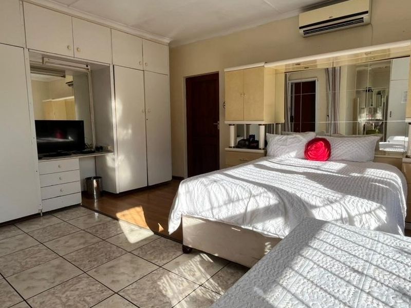 Spacious bedroom featuring extensive built-in cabinetry, a wall-mounted air conditioning unit, and a combination of tiled and laminate flooring.