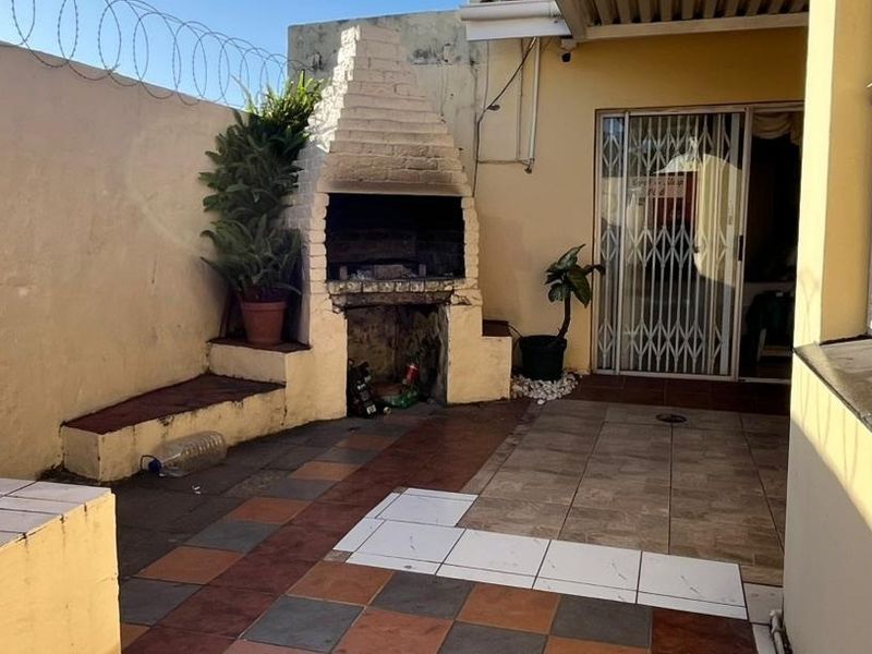 Outdoor patio area featuring a built-in brick braai, tiled flooring, and secure perimeter walling with razor wire.