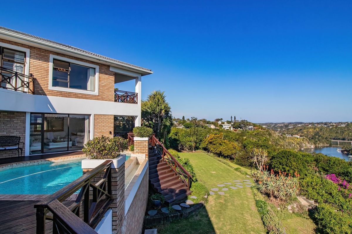 Rear exterior view featuring a swimming pool, timber decking, and a balcony overlooking a landscaped garden and river landscape.