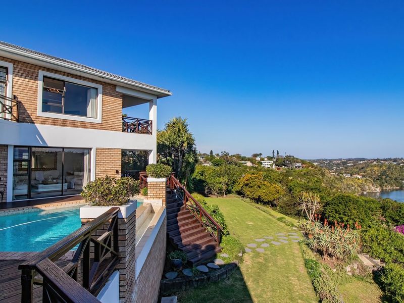 Rear exterior view featuring a swimming pool, timber decking, and a balcony overlooking a landscaped garden and river landscape.