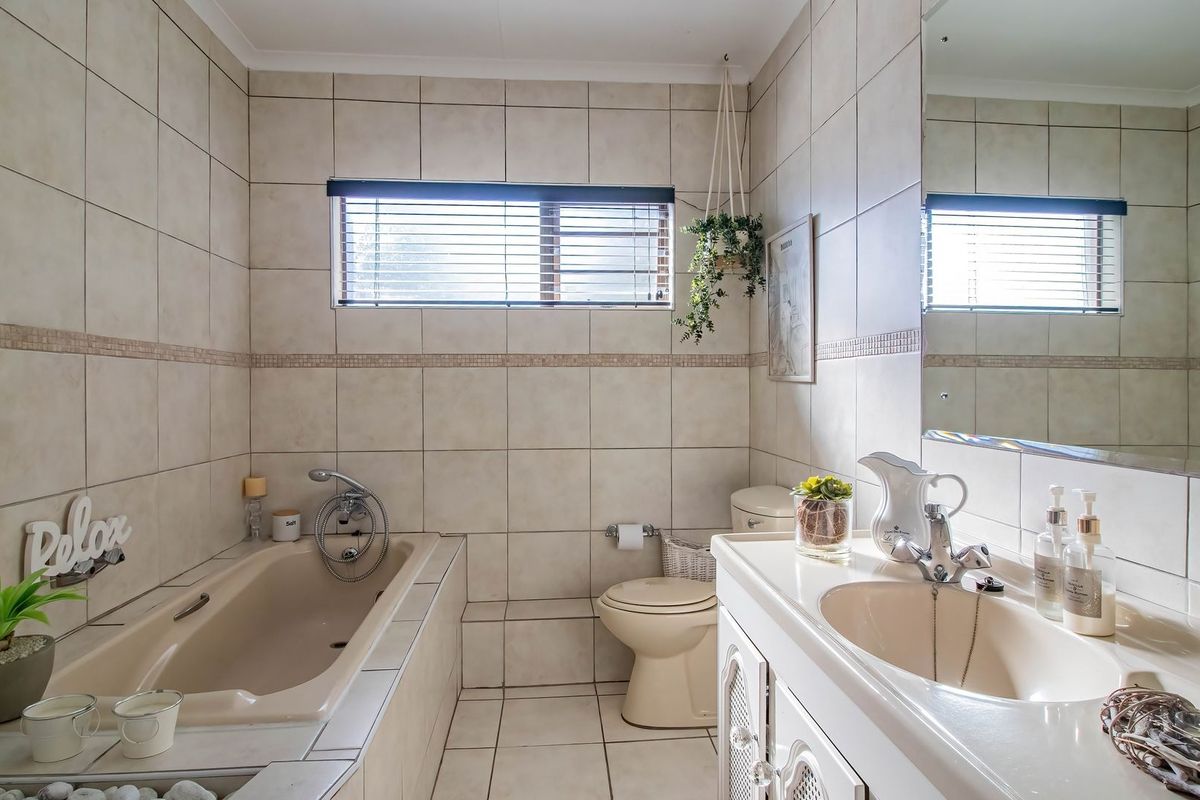 A functional bathroom featuring a built-in bathtub, vanity cabinet with integrated sink, toilet, and neutral wall tiling.