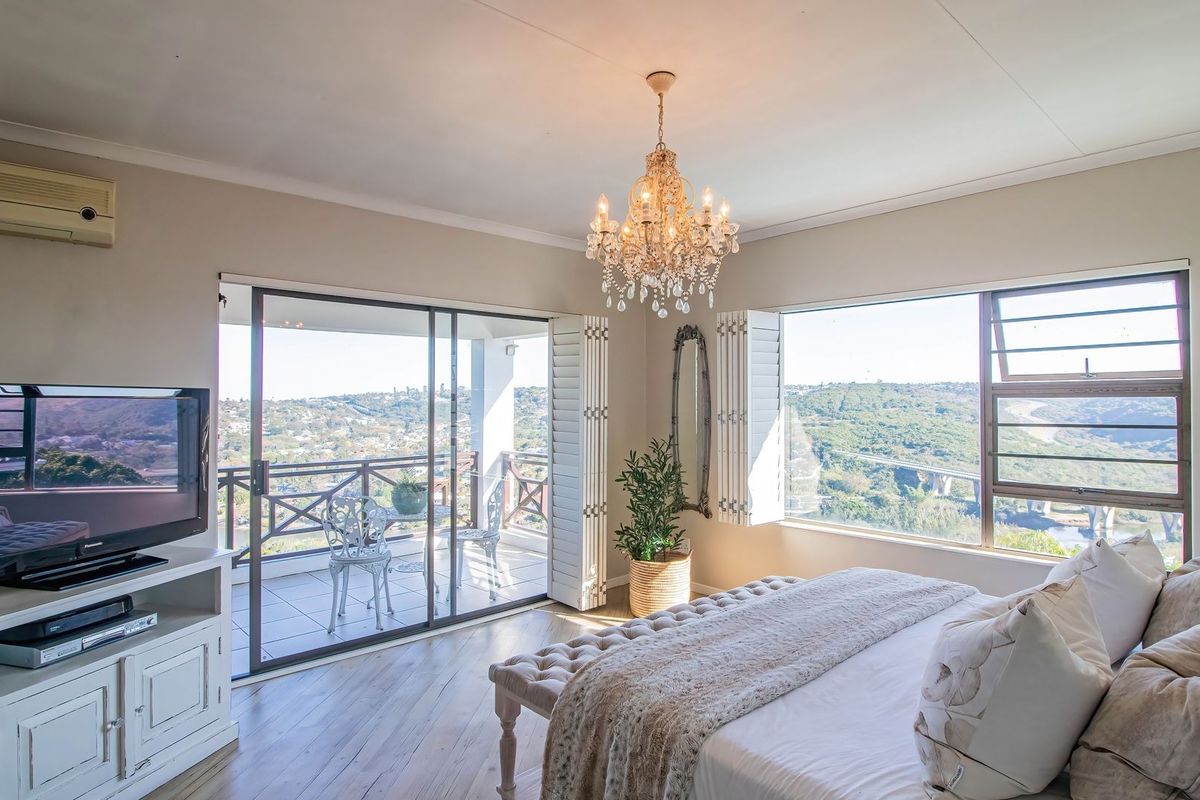 Spacious bedroom featuring laminate flooring, plantation shutters, a crystal chandelier, and direct access to a private balcony with scenic views.