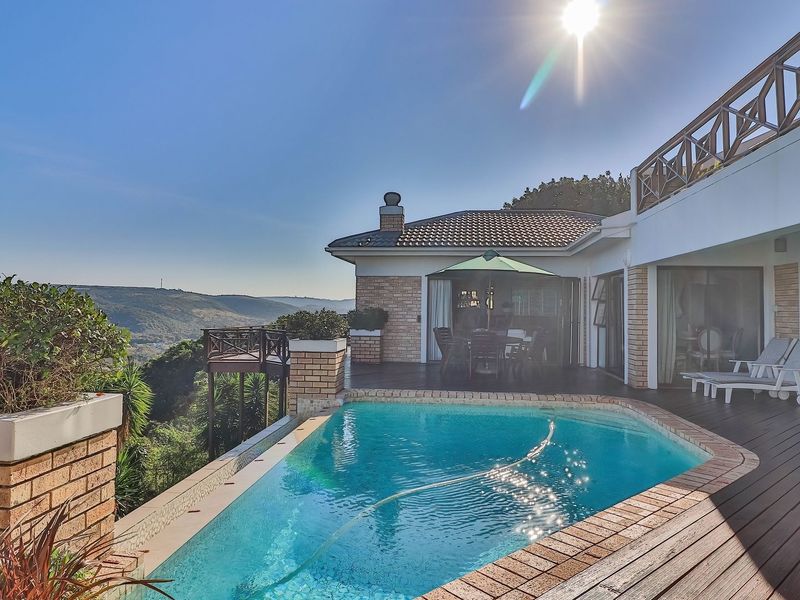 Outdoor pool area featuring timber decking, brick planter boxes, and a scenic elevated view of the surrounding landscape.