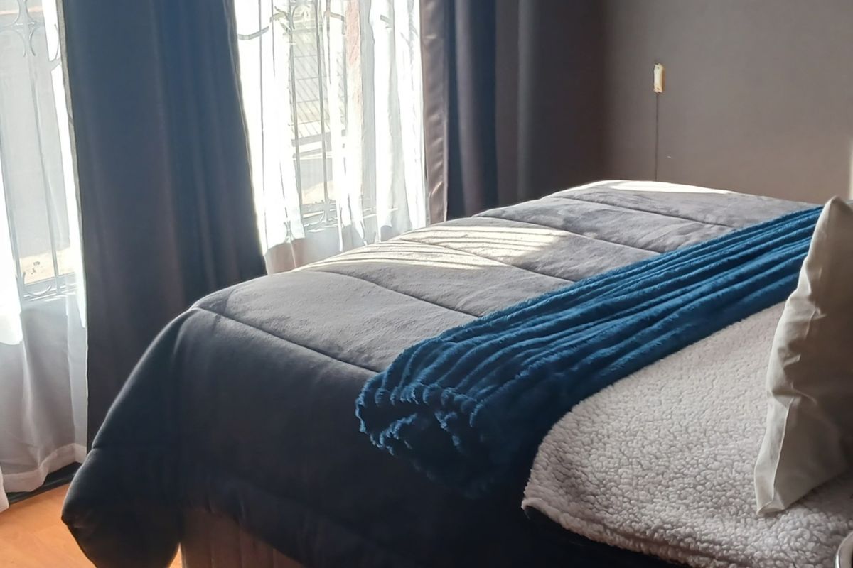A bedroom featuring laminate flooring and natural light entering through a window with curtain rails.