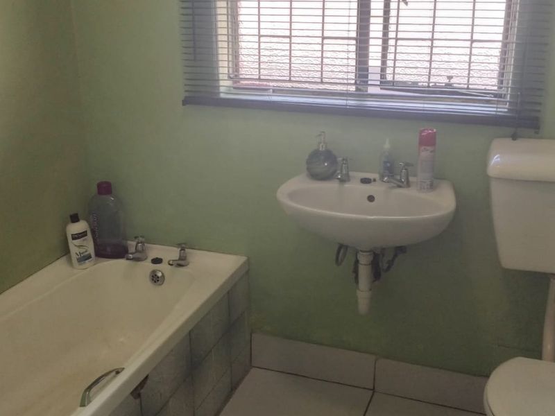 A functional bathroom featuring a bathtub, wall-mounted basin, and toilet, with dated finishes and green wall paint.
