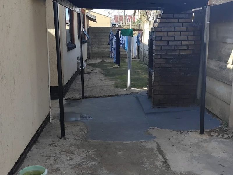 Rear exterior area featuring a built-in brick braai, covered patio space, and concrete flooring, enclosed by precast boundary walls.